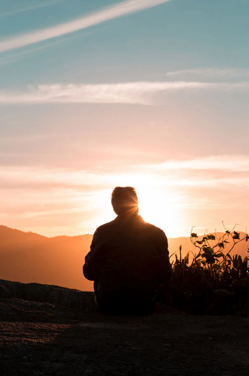 Person sitting outdoors at sunrise, reflecting on life and mental wellbeing during OCD recovery