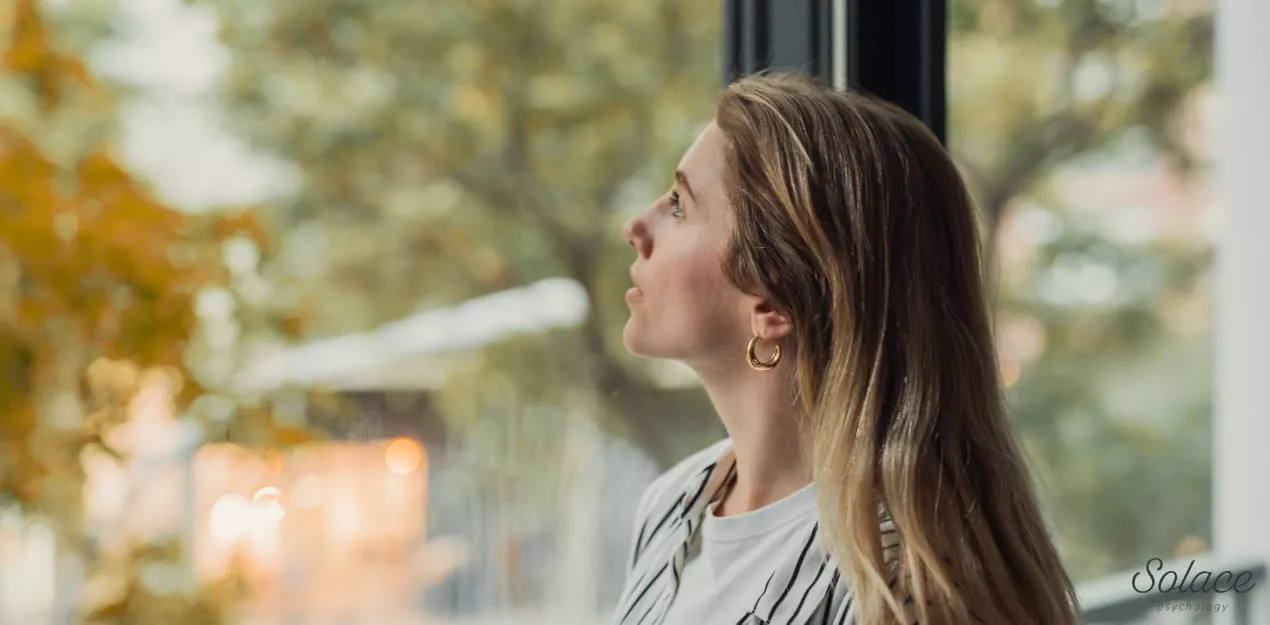 3-3-3-rule-grounding-technique-anxiety Woman sitting calmly by a window, practising a grounding technique to manage anxious thoughts